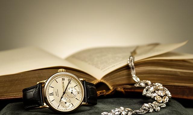 Fine collectible watch, jewellery and antique book displayed under soft gallery lighting